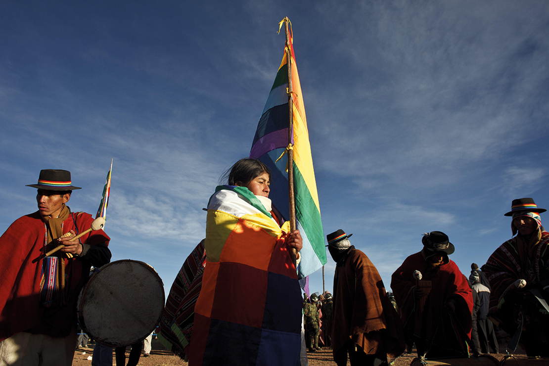 A woman holds a flag representing the indigenous peoples of Latin America in Tiahuanaco, Bolivia. Credit: mauritius images GmbH